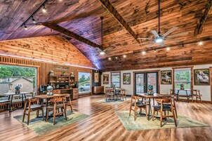 A spacious dining area with wooden tables and chairs, a bar area with shelves, and large windows offering views of the outdoors.