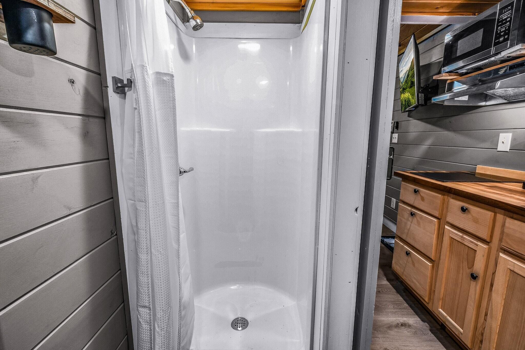 Baño con ducha, armarios de madera y un microondas.