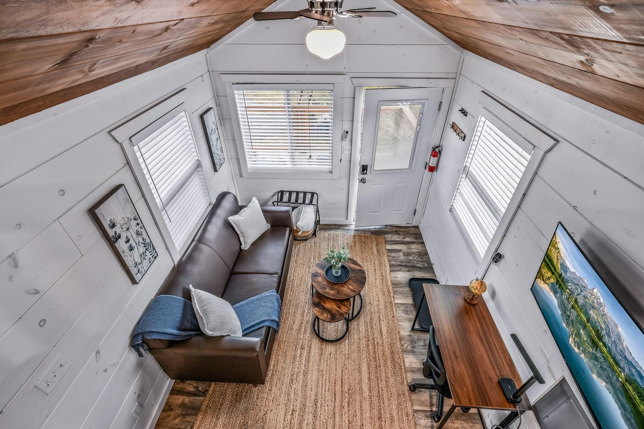 A compact living space with a brown leather sofa, a round coffee table, and a flat-screen TV mounted on the wall.
