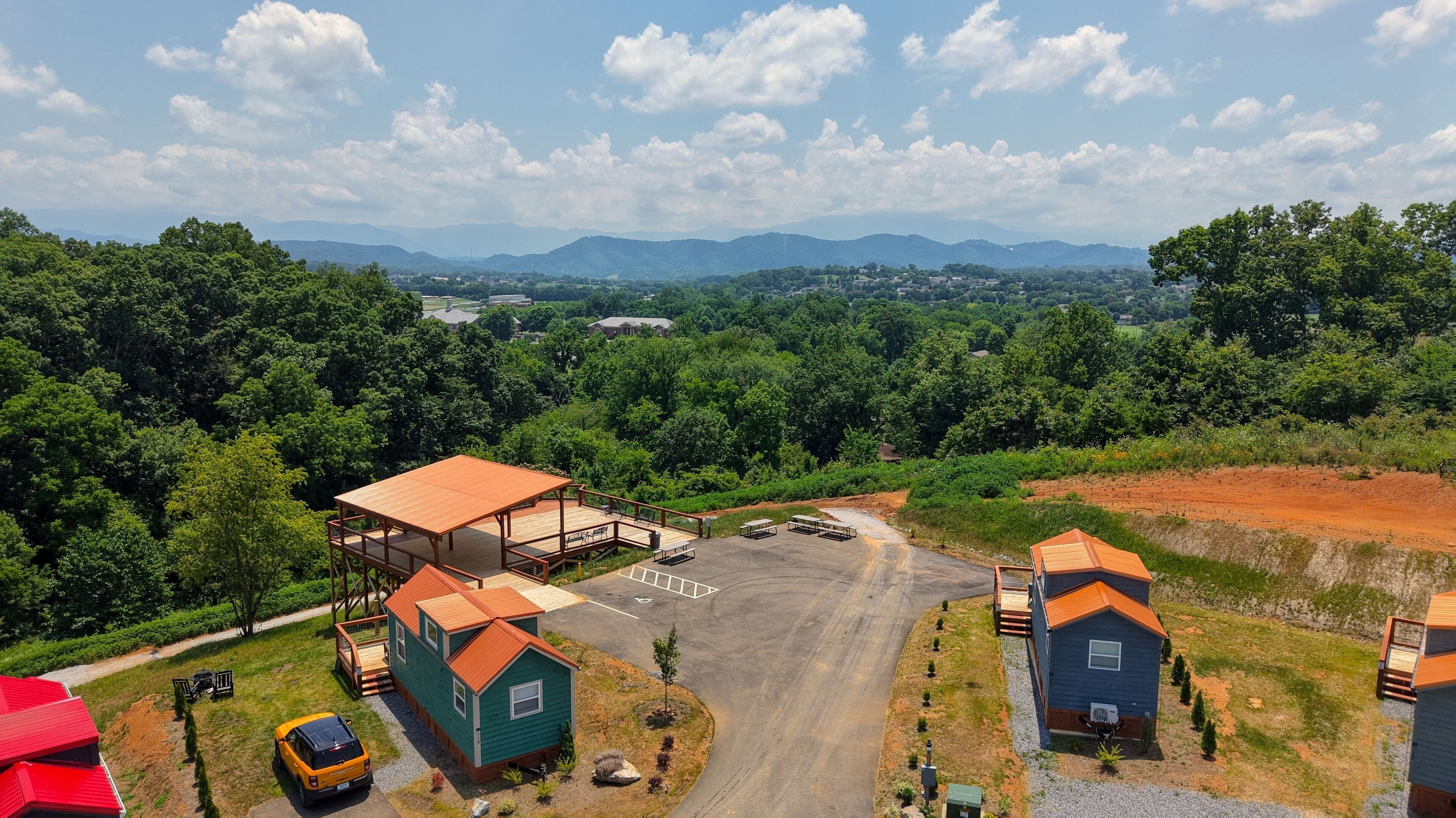 A view of a parking lot with several small cabins, a yellow car, and a red building in the foreground.