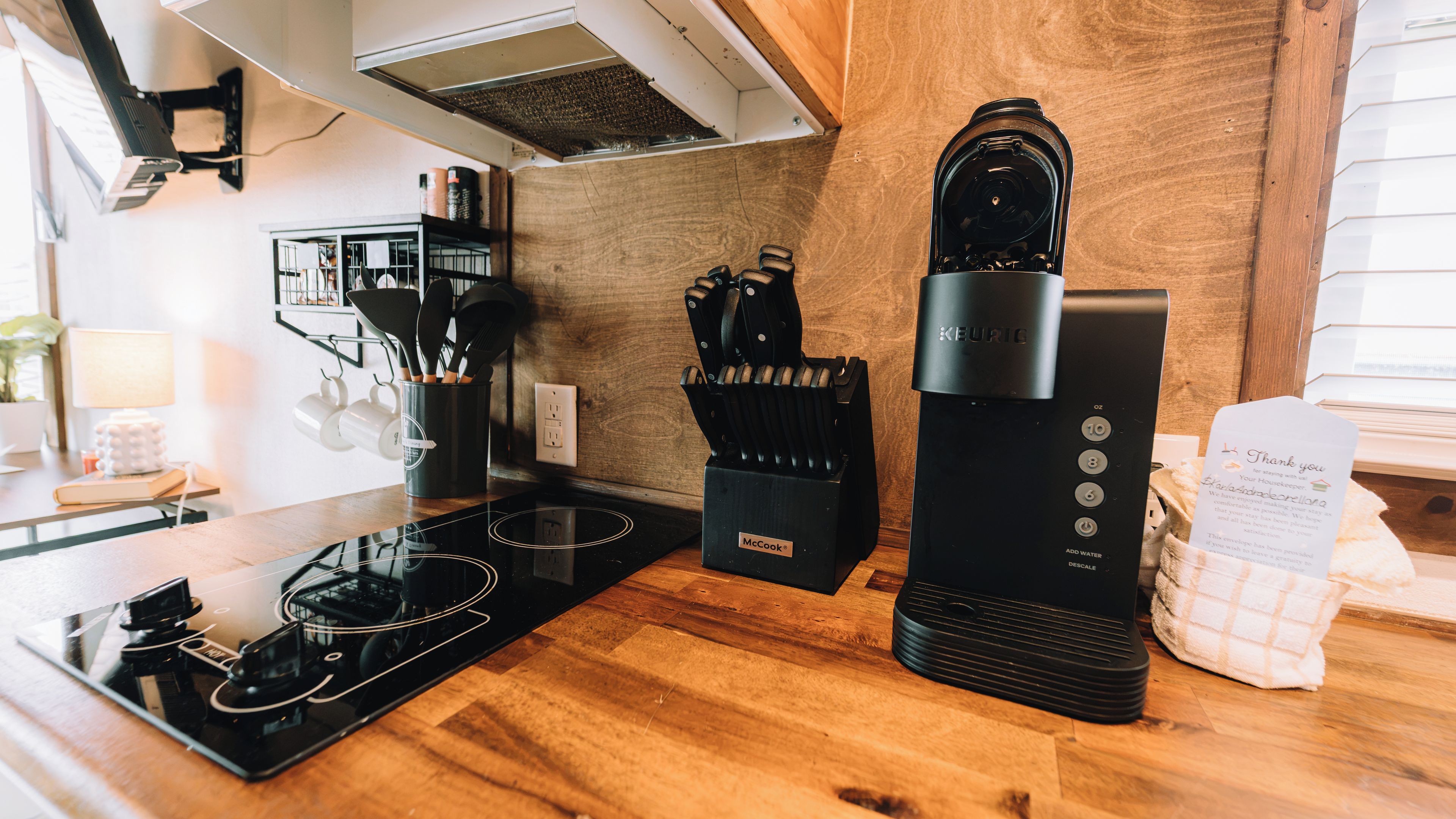 Een moderne keuken met een zwarte Keurig koffiemachine, een blok messen van McCook en een waterkoker op een houten aanrecht.