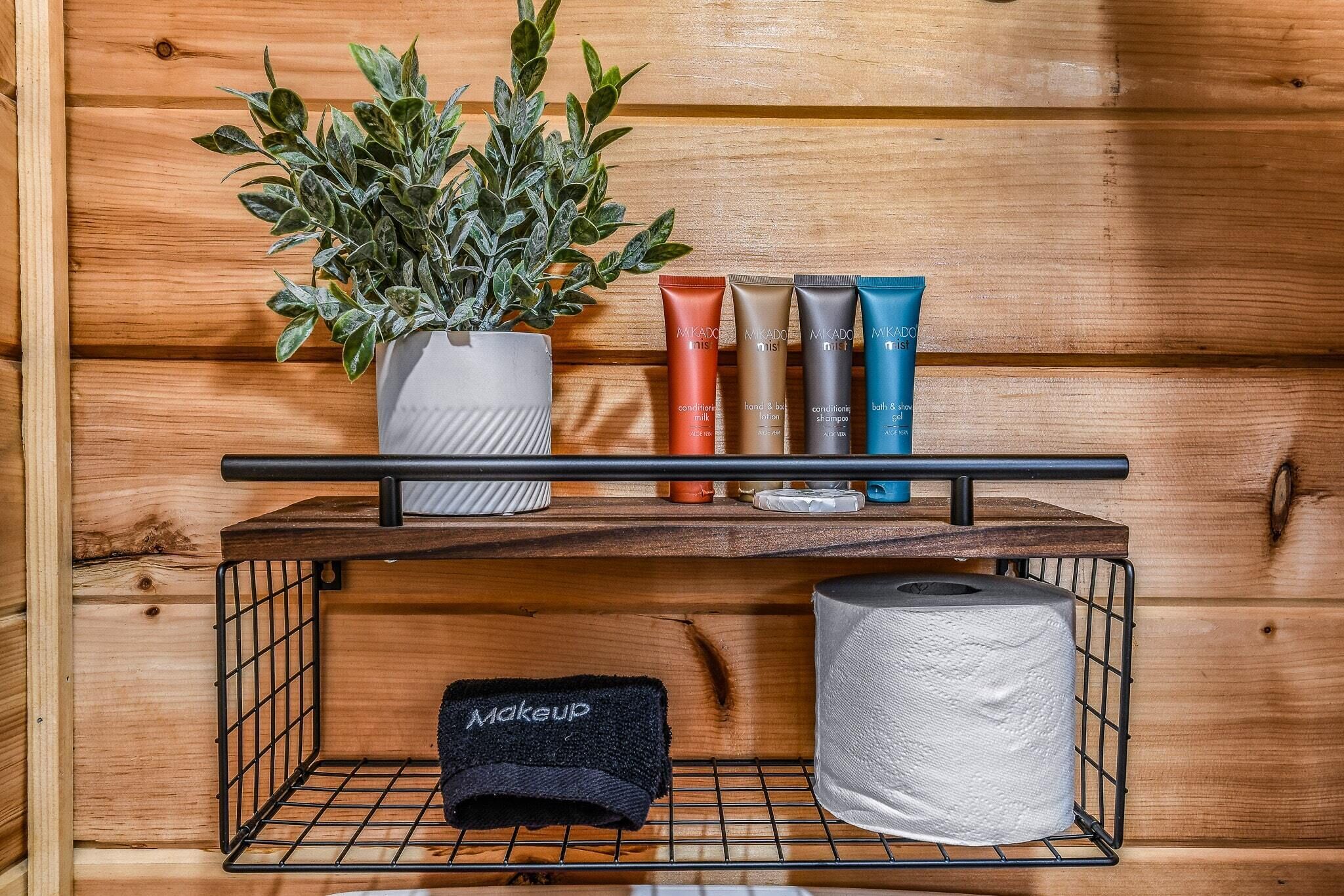 A wooden shelf with makeup products, a potted plant, and a tissue roll.