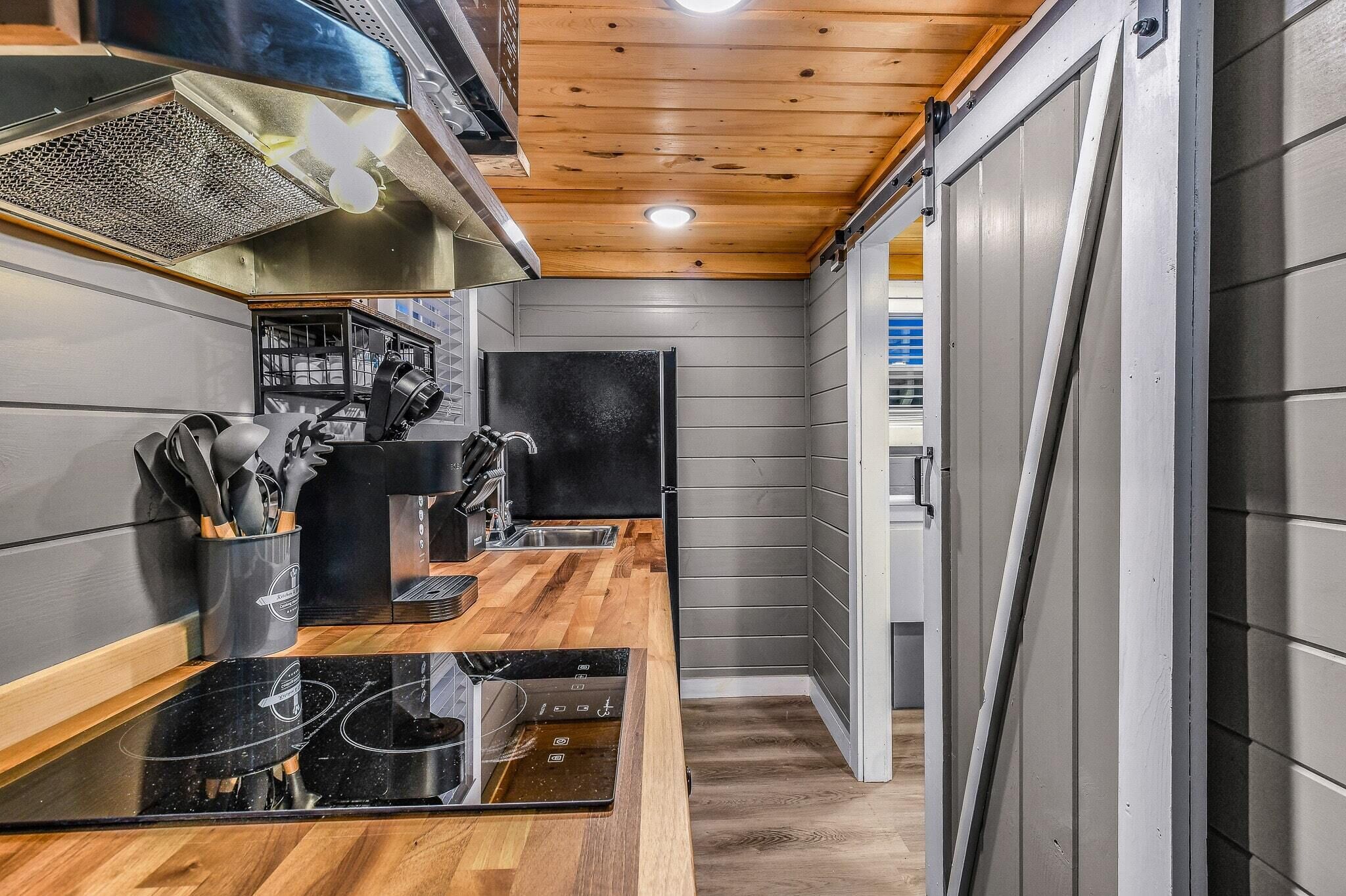 A narrow kitchen with wooden countertops, a black stove, and a grey wall.