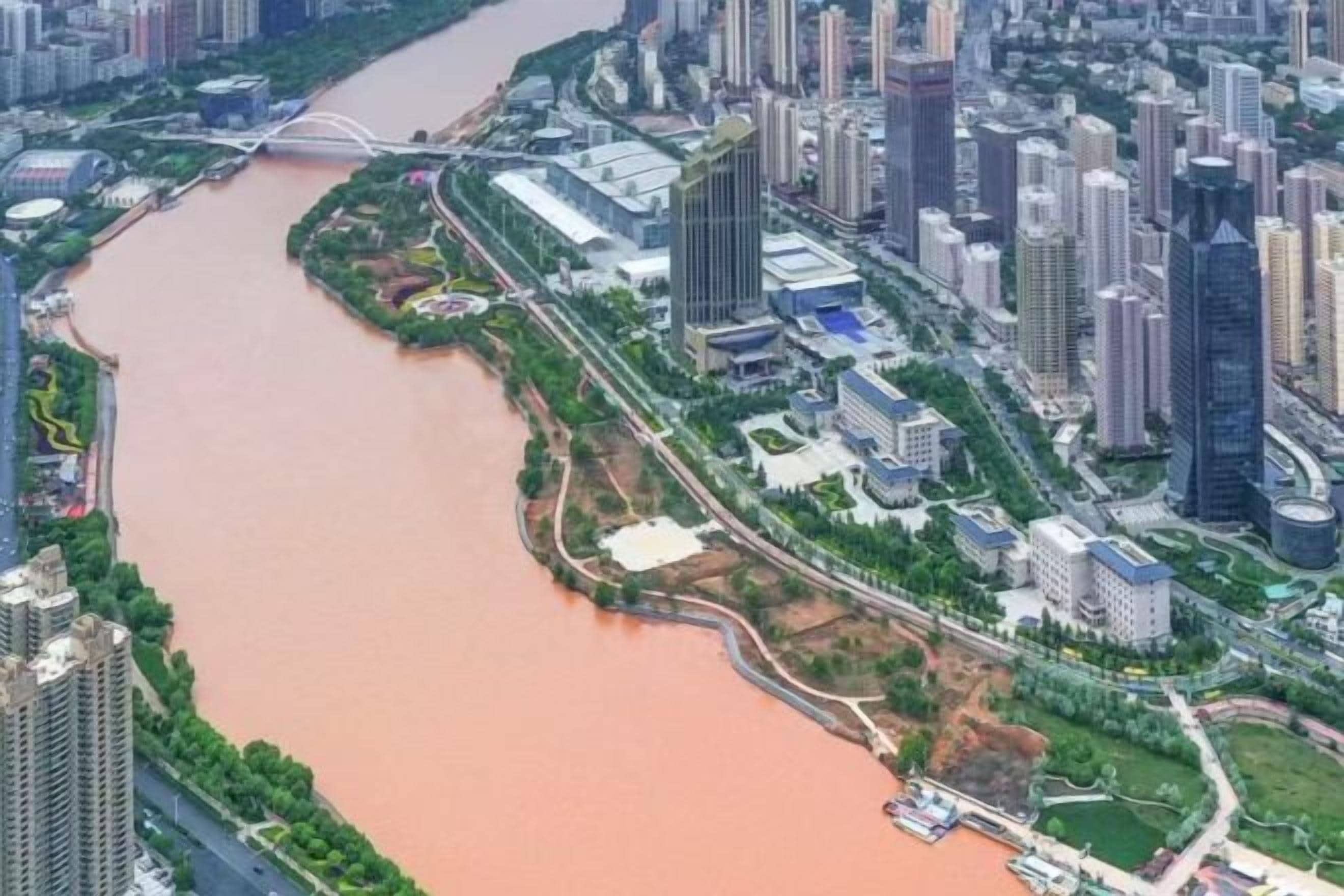A river running through a city with high-rise buildings on one side and a bridge crossing the river.