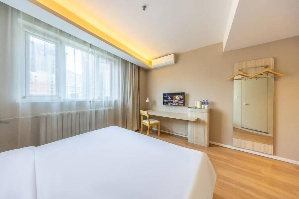 Habitación de hotel con cama, escritorio, silla, televisor, armario y ventana con cortinas.