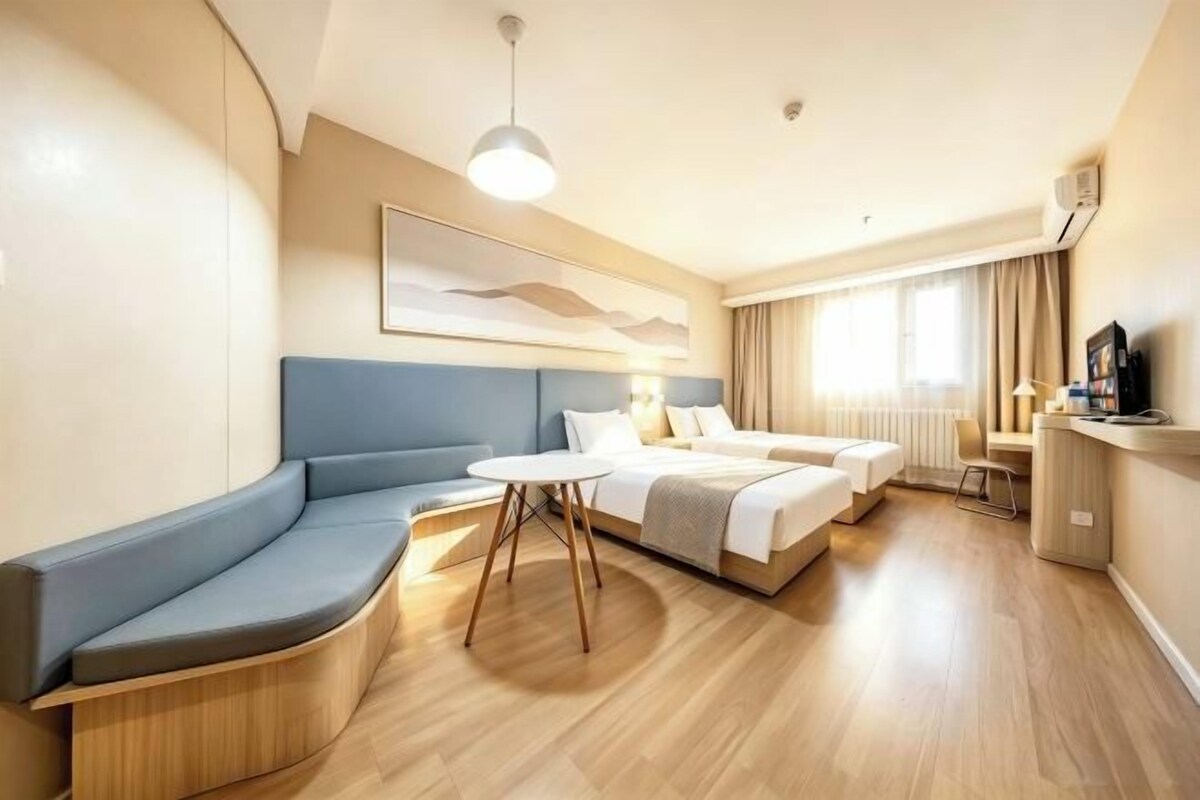 A modern hotel room with a curved seating area, a bed, a small table, and a television.