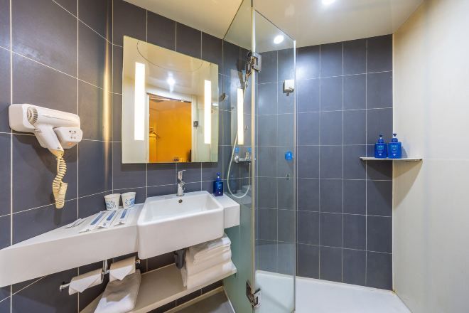 Une salle de bain moderne équipée de deux lavabos, d’un sèche-cheveux, d’un miroir et d’une cabine de douche.