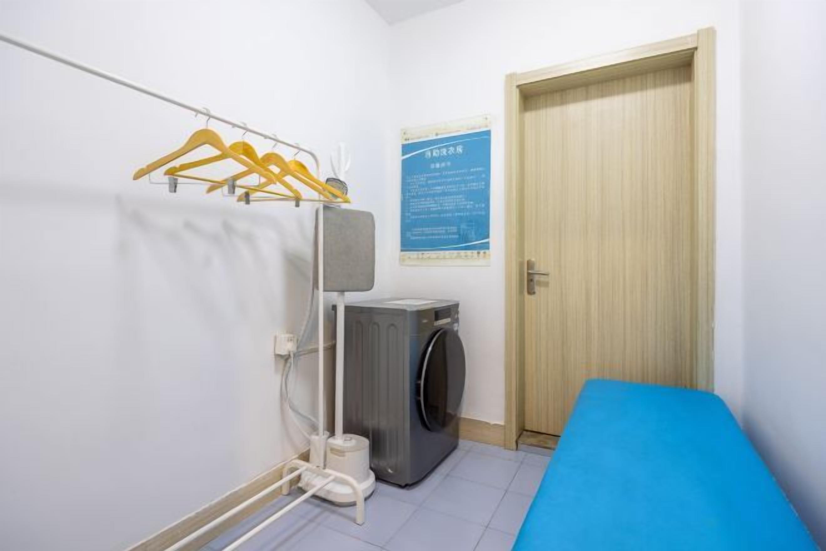 Une petite pièce avec un matelas bleu, un lave-linge et une porte en bois.