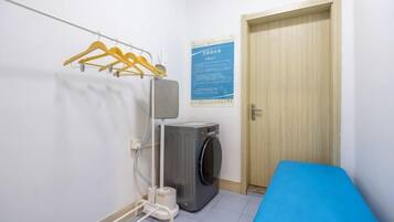 Une petite pièce avec un matelas bleu, un lave-linge et une porte en bois.