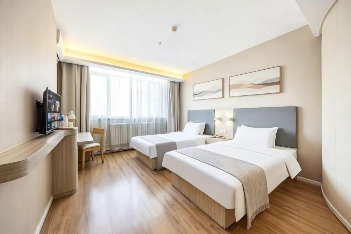 A hotel room with two beds, a desk, a television, and a window with curtains.