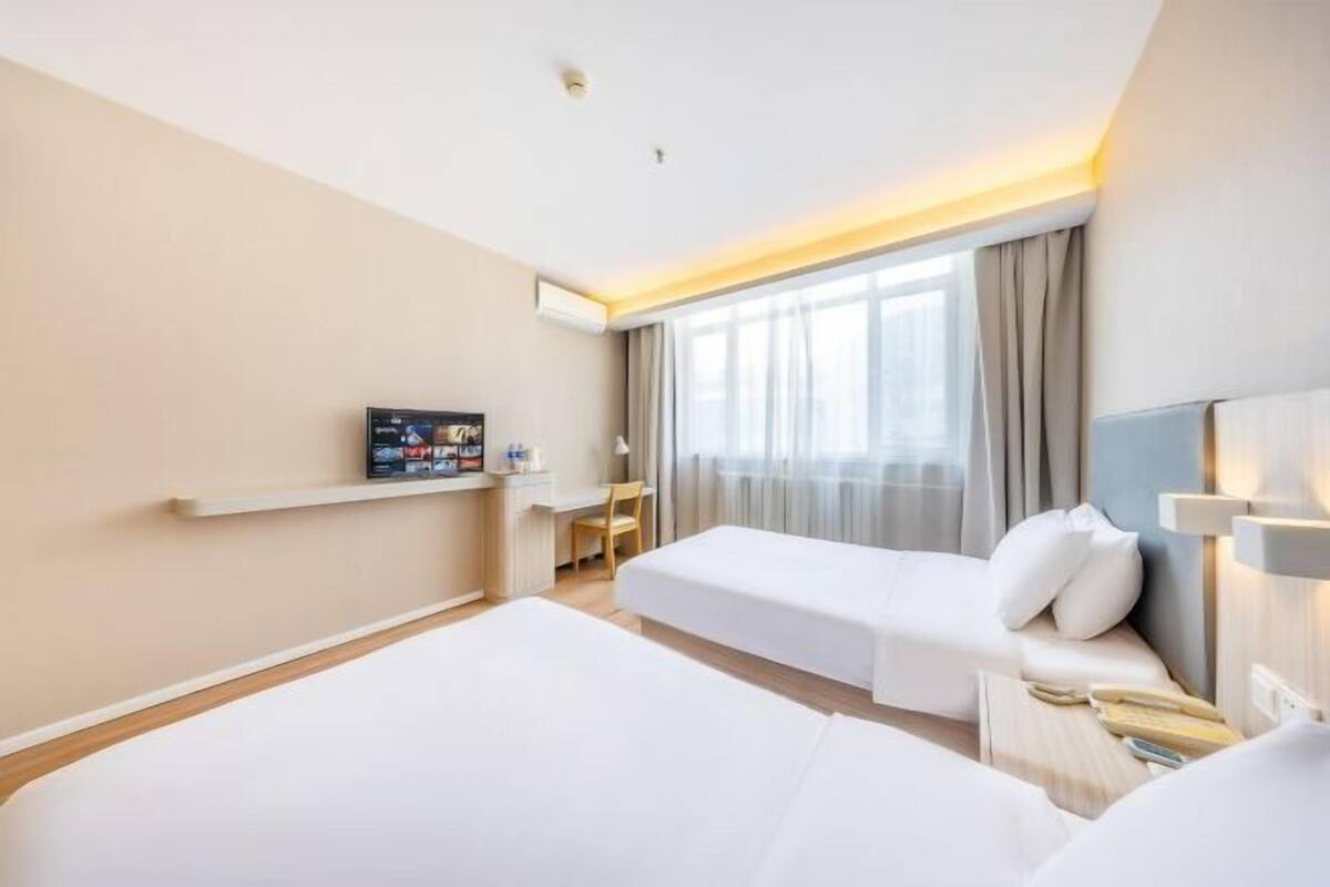 Habitación de hotel con dos camas, un escritorio, un televisor y una ventana con cortinas.