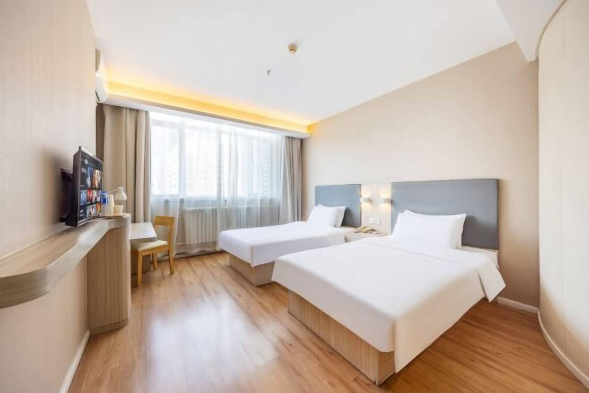 Habitación de hotel con dos camas, un escritorio, una silla y un televisor.