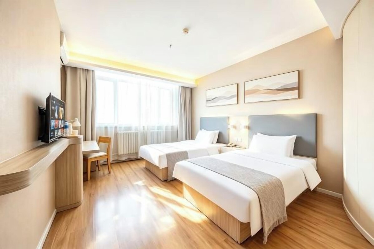 A hotel room with two beds, a desk, a chair, and a television.