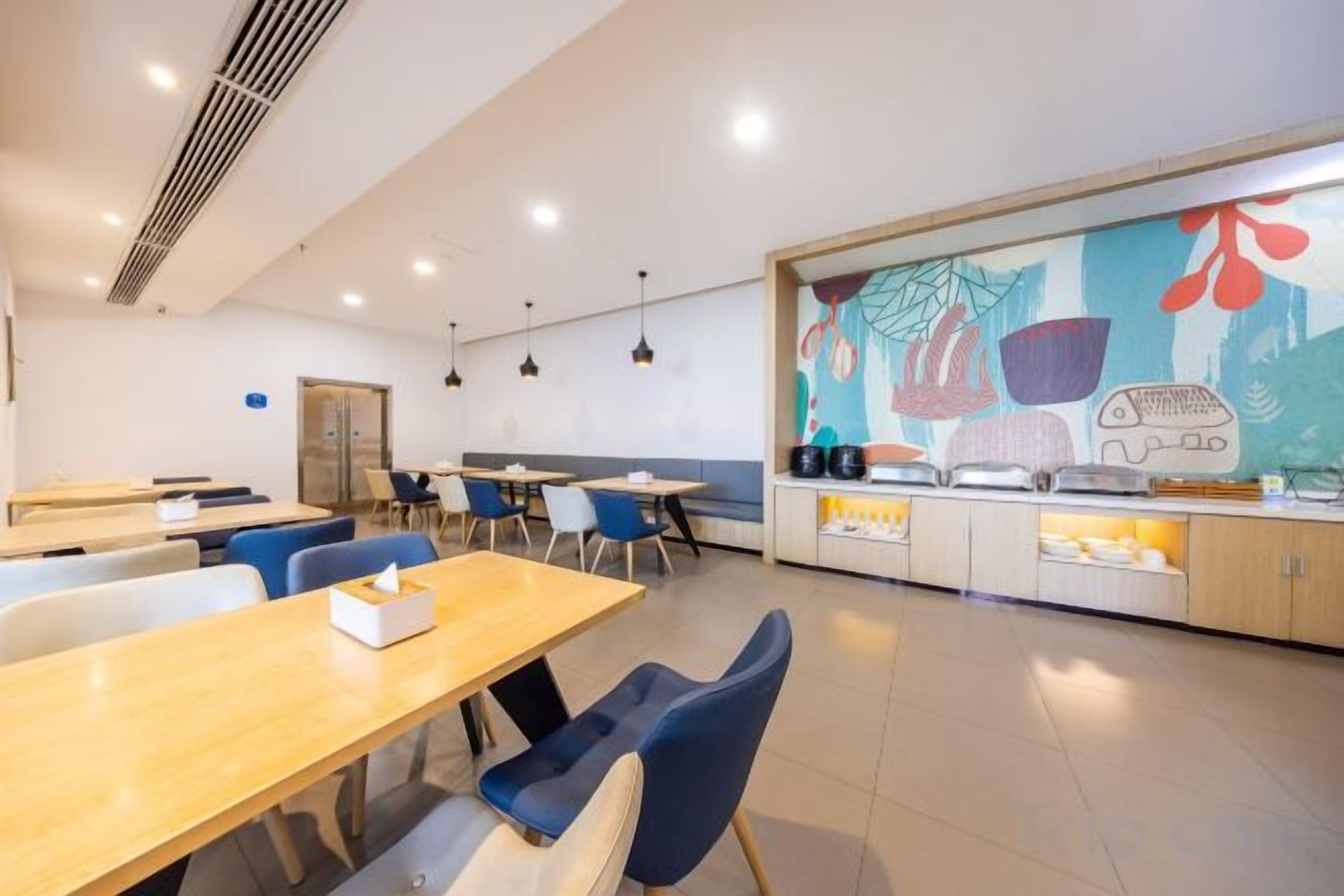 Un espace repas moderne avec des tables et des chaises, un comptoir de cuisine et une fresque colorée sur le mur.