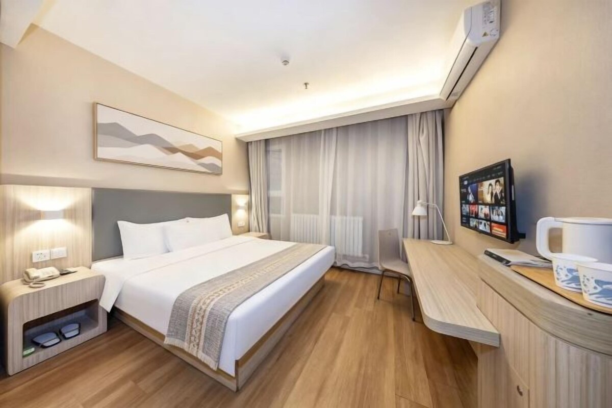 A hotel room with a bed, bedside table, lamp, and a desk with a chair.
