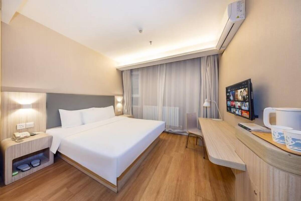 Una habitación de hotel con una cama, mesita de noche, lámpara y un pequeño escritorio con silla.