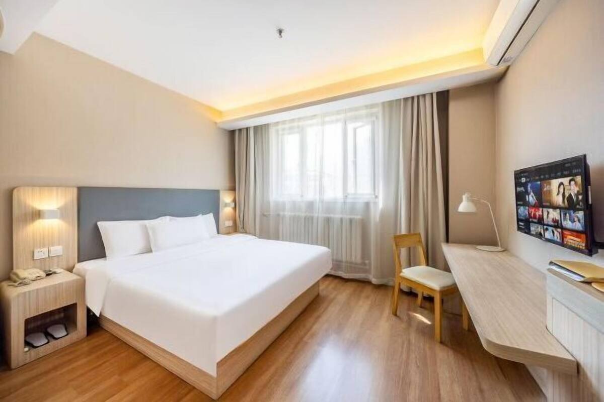 Habitación de hotel con cama, escritorio, silla, mesita de noche y televisión montada en la pared.