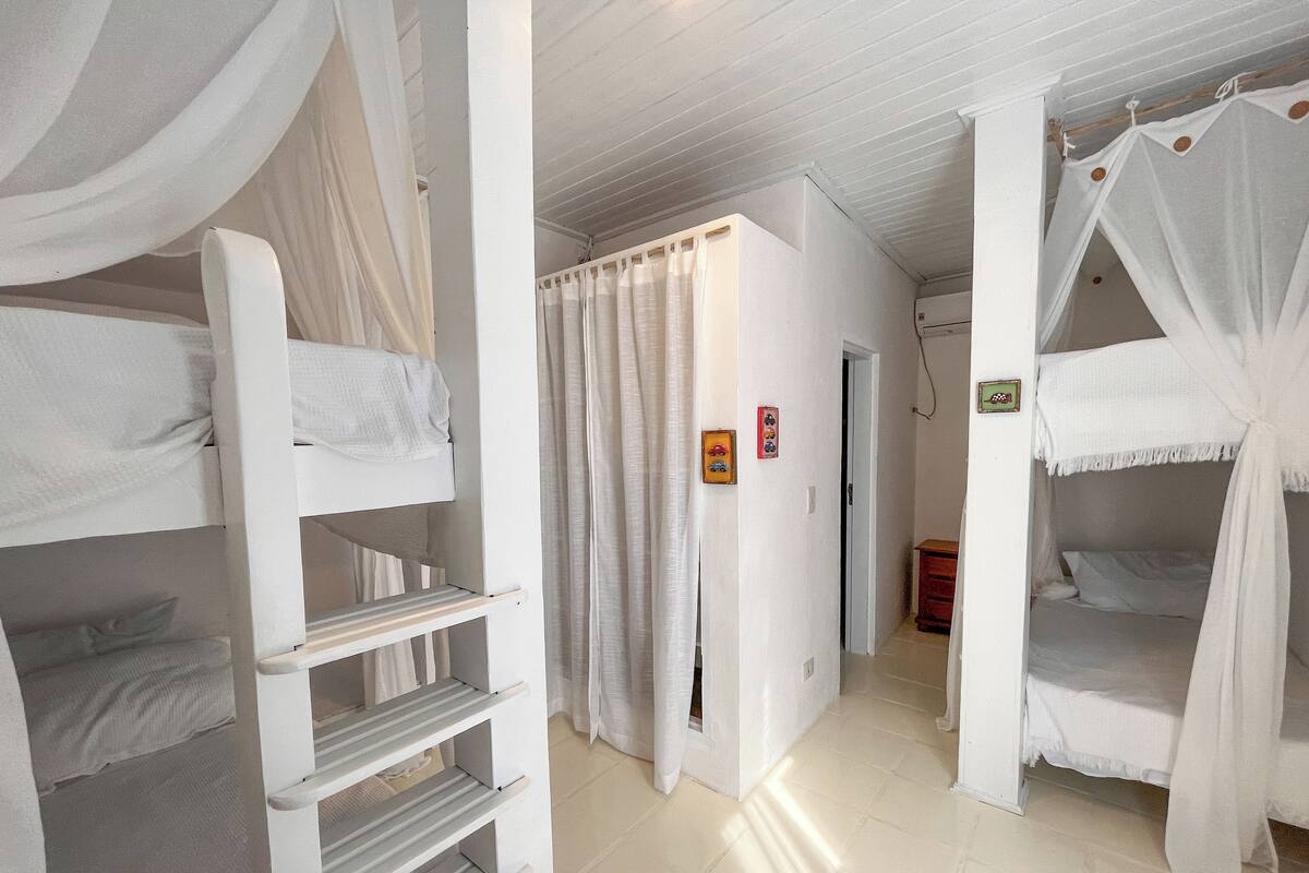 Une chambre avec des lits superposés, une armoire blanche et une porte qui donne sur une autre pièce.