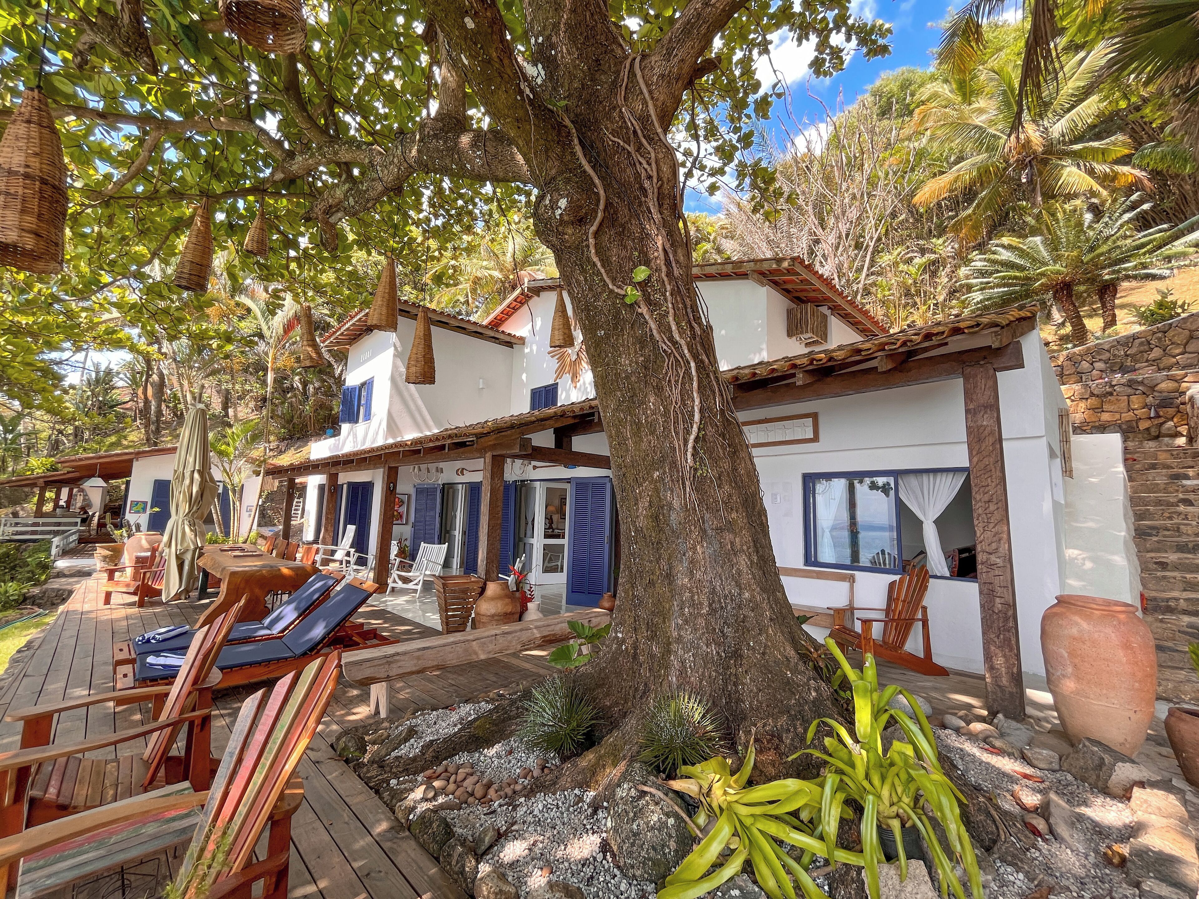 A villa with a wooden deck, outdoor seating, and a large tree.