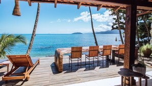 A wooden deck with a view of the ocean, a wooden table, and chairs. - Blow Show Casa I  (Ilhabela)
