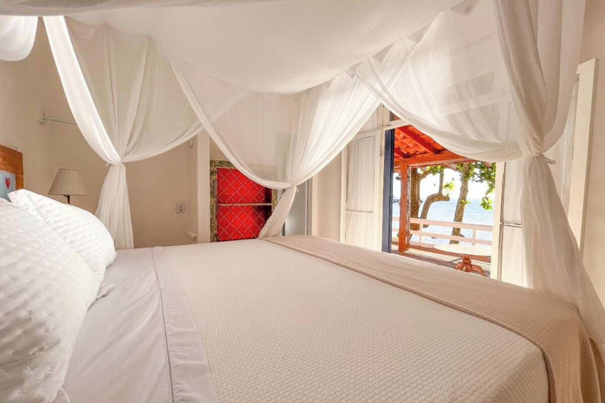 Une chambre à coucher avec un lit, des rideaux blancs et une vue sur la mer.