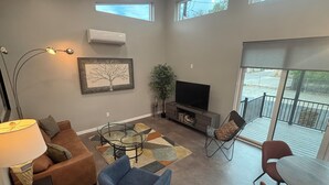 A living room with a sofa, armchair, TV, and a glass coffee table. - Dramatic New Home Right Downtown (Prescott)