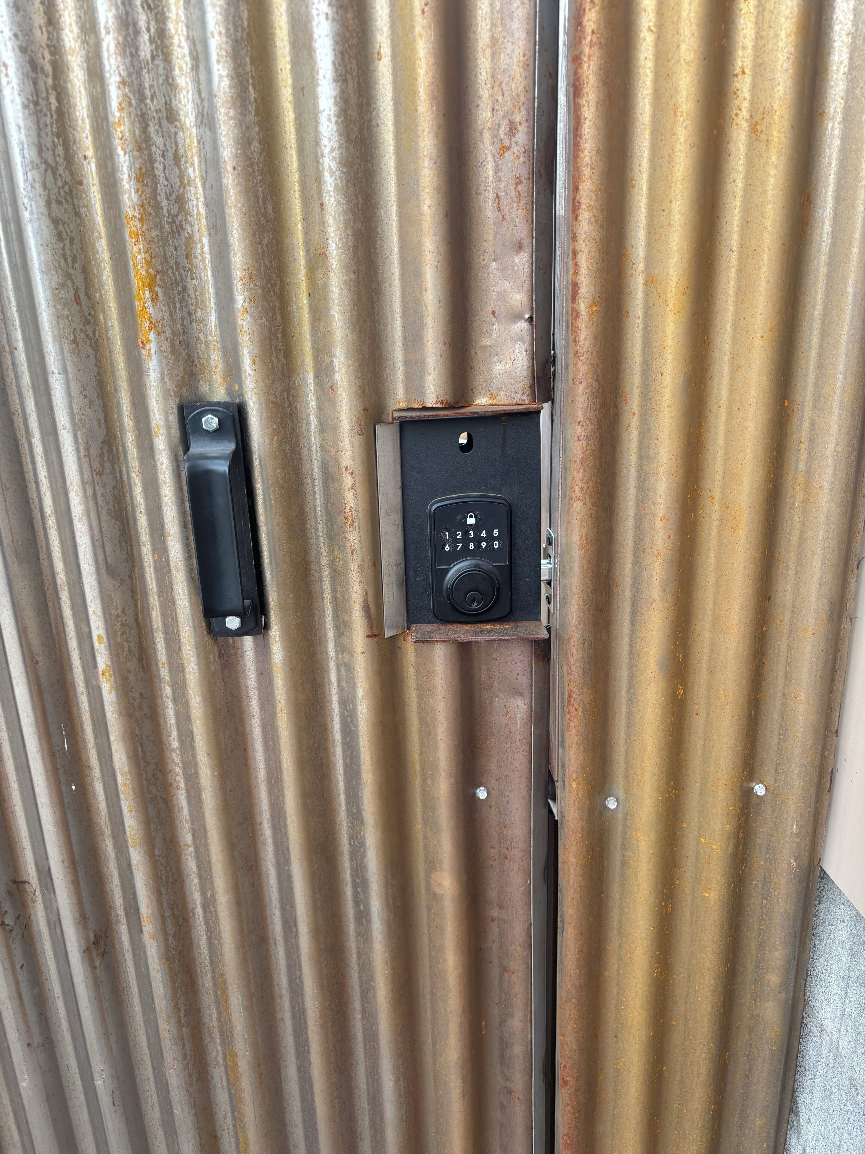 Una puerta metálica con un teclado electrónico y un pequeño objeto rectangular adherido.