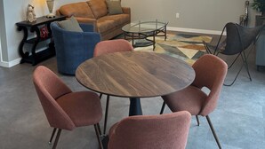 A modern living room with a round wooden table, four cushioned chairs, a sofa, a glass coffee table, and a chandelier. - Dramatic New Home Right Downtown (Prescott)