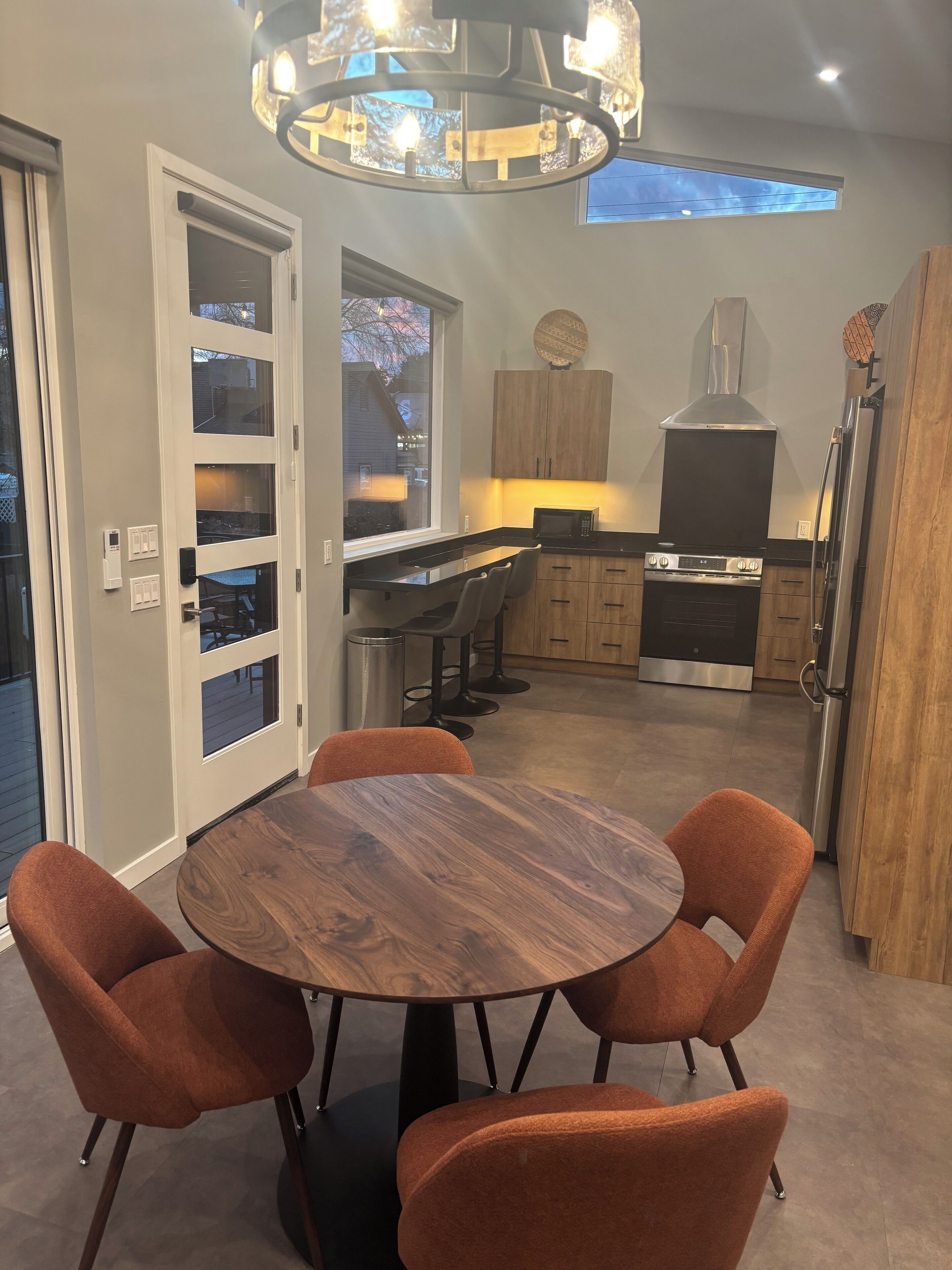 A modern kitchen with a dining area, featuring a round wooden table with four chairs, a built-in oven, and a stainless steel refrigerator.