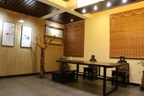 A room with a wooden floor, a dining table with chairs, a decorative tree, and framed artwork on the walls. - Gujia Hotel (Kunming)