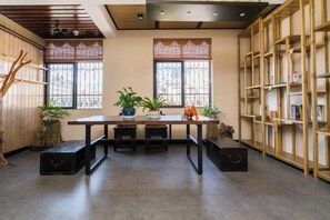 A room with a wooden table, benches, a bookshelf, and potted plants. - Gujia Hotel (Kunming)