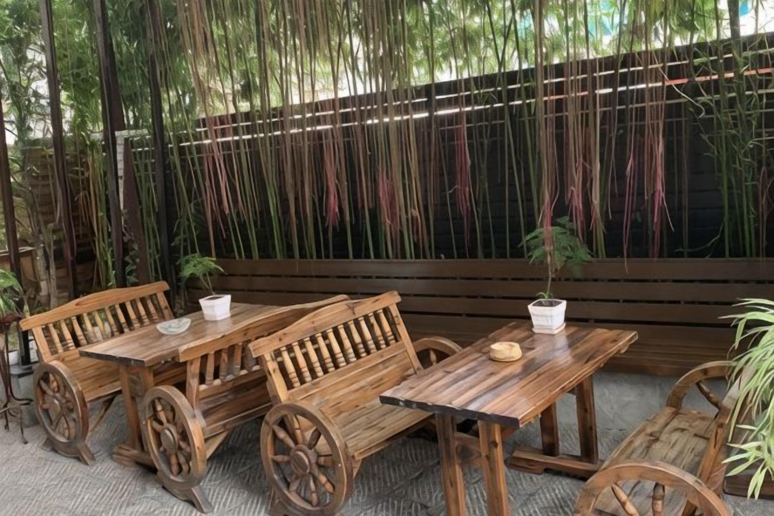 Outdoor wooden tables and benches with wheels, surrounded by a bamboo fence.