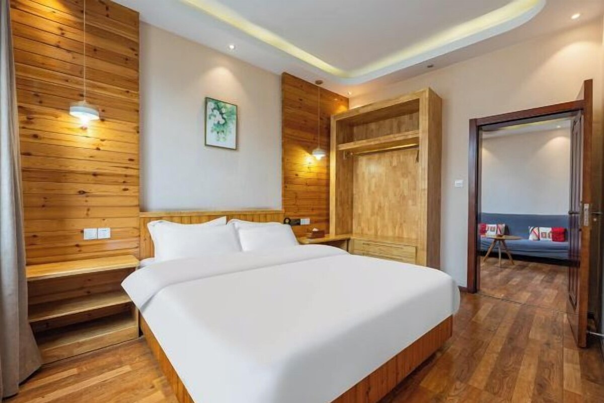 A modern hotel room with a wooden wall panel, a bed with white linens, a wooden wardrobe, and a small table with a chair.