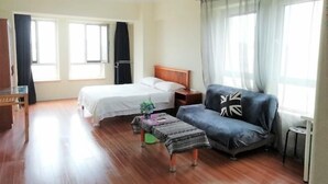 A room with a bed, a sofa, a small table, and a window with curtains. - Xingfu Apartment Hotel (Dalian)