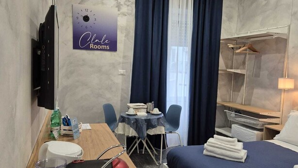 A hotel room with a bed, a desk, a chair, a small table, a TV, and a sign on the wall. - Clale Rooms (Naples)