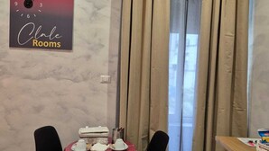 A hotel room with a bed, a table with a red tablecloth, two chairs, an air conditioning unit, and a window with curtains. - Clale Rooms (Naples)