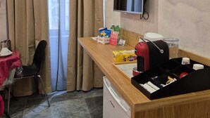 A compact hotel room with a wooden desk, a television mounted on the wall, a small table with a chair, and a window with beige curtains. - Clale Rooms (Naples)