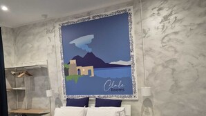 A hotel room with a bed, a side table, a lamp, and a painting of a landscape. - Clale Rooms (Naples)