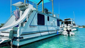 Eine große, weiße Yacht mit dem Namen „AQUA CRUISER 35“ liegt in einer Marina mit klarem, türkisblauem Wasser vor Anker.