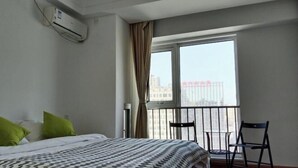 A hotel room with a bed, a window with a view of buildings, and an air conditioning unit on the wall. - Yisuli Hotel (Dalian Hi-tech Wanda Plaza) (Dalian)