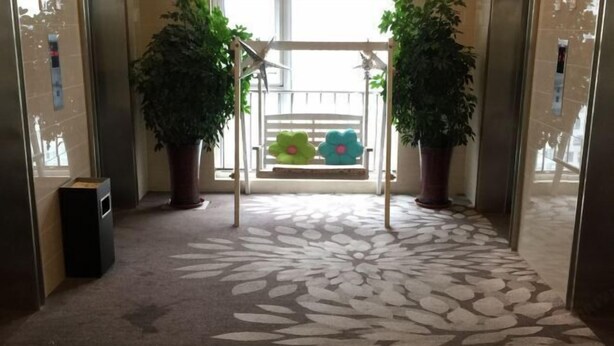 A hallway with a patterned carpet, a swing with flower-shaped cushions, and potted plants on either side. - Yisuli Hotel (Dalian Hi-tech Wanda Plaza) (Dalian)