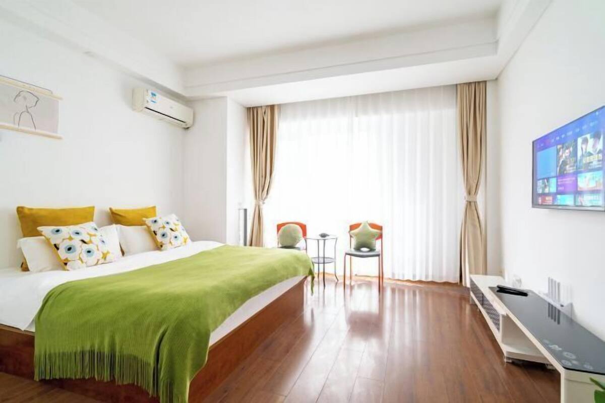 A hotel room with a bed, a desk, two chairs, an air conditioning unit, and a TV on the wall.