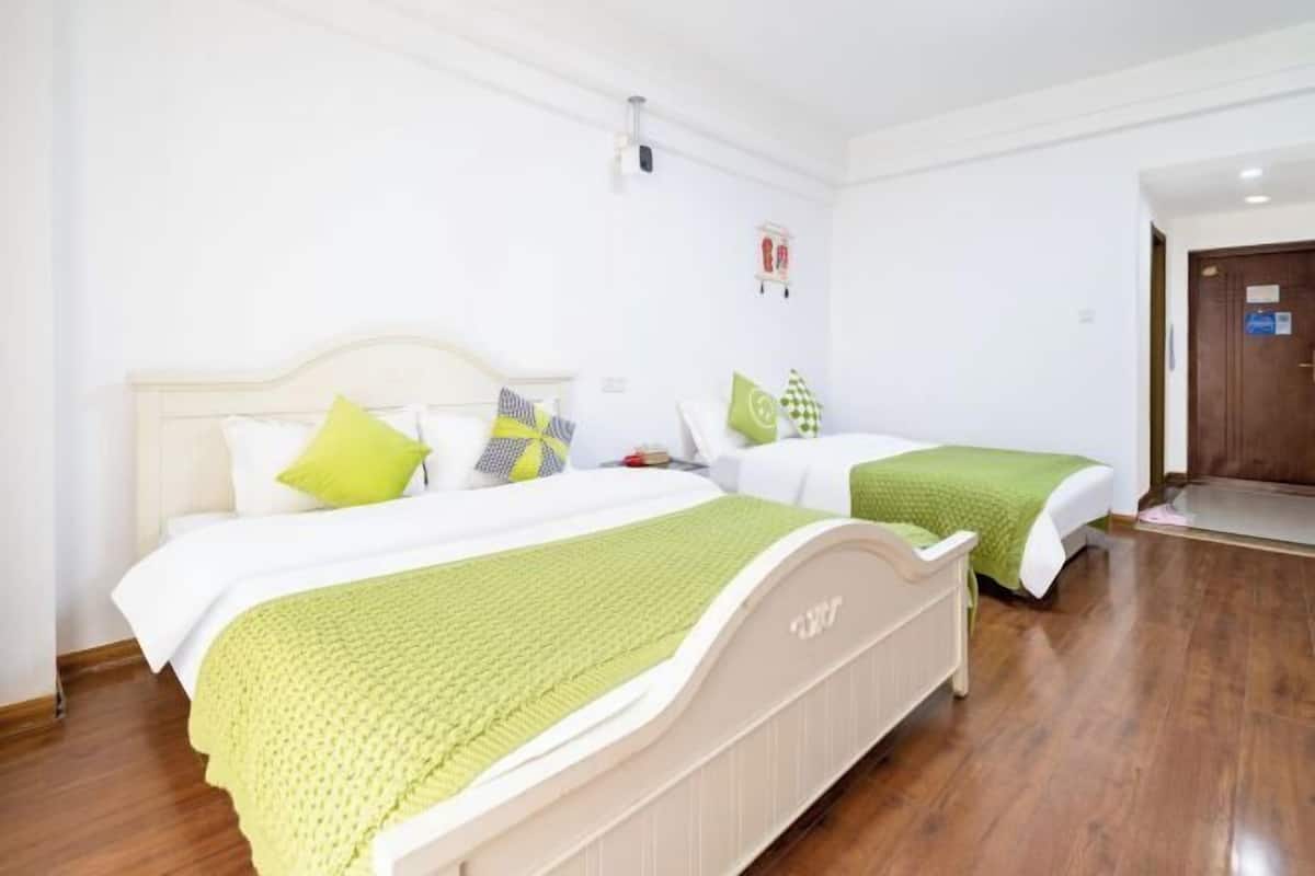 A hotel room with two beds, a wooden floor, a white wall, and a door.