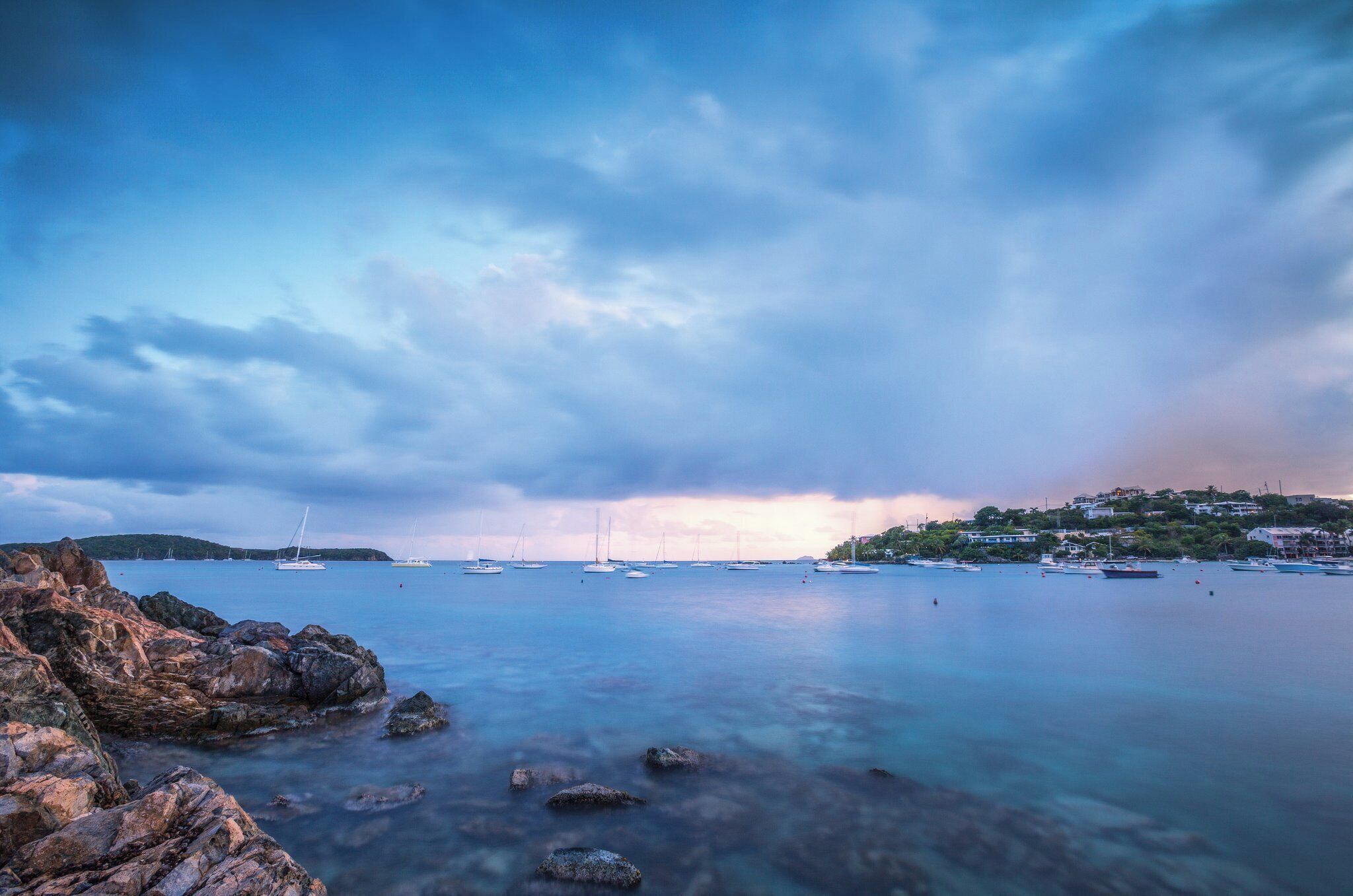 A coastal scene with boats, rocky shoreline, and a distant town.