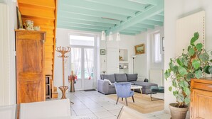 A living room with a sofa, a blue armchair, a wooden cabinet, and a potted plant. - L'Embrun - Accès direct plage - Jardin (La Bernerie-en-Retz)