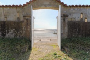 An open doorway leading to a beach with a concrete wall and a tiled roof.