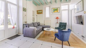 A living room with a grey sofa, a blue armchair, a coffee table, and a TV. - L'Embrun - Accès direct plage - Jardin (La Bernerie-en-Retz)