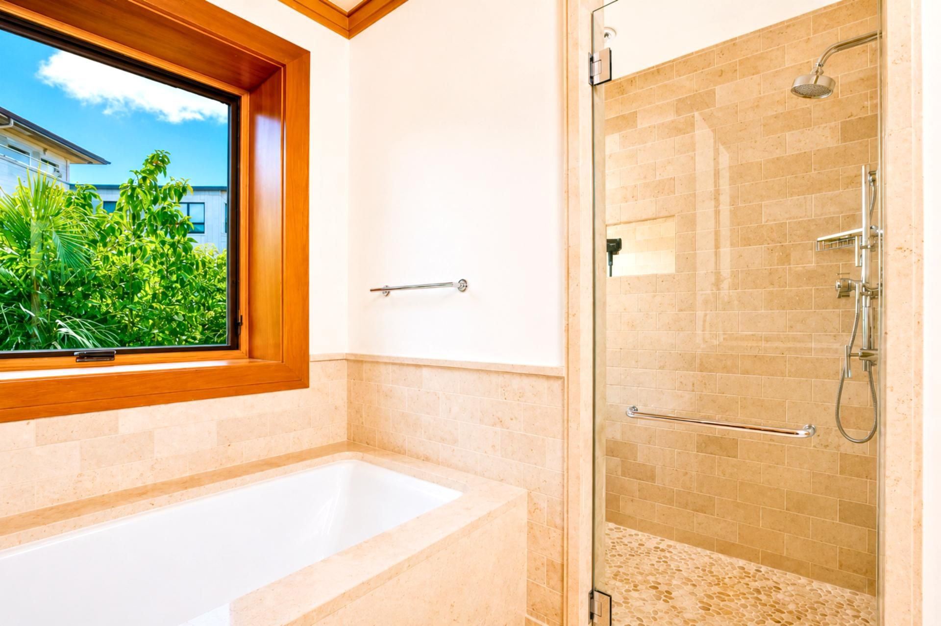 Een badkamer met een bad, een douchecabine van glas en een raam met uitzicht op groen.