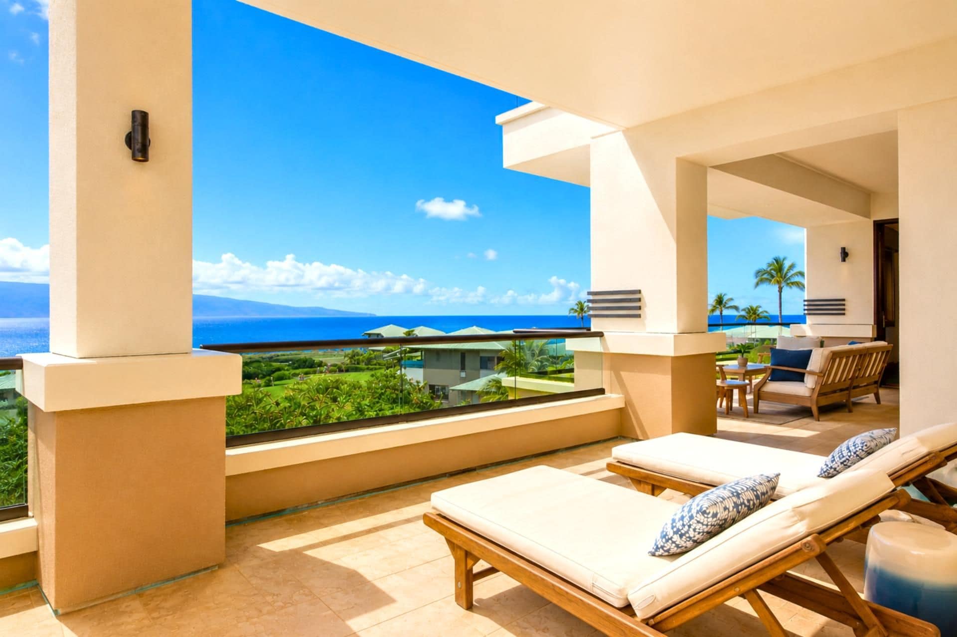 A balcony with a view of the ocean, lounge chairs, and a table with chairs.