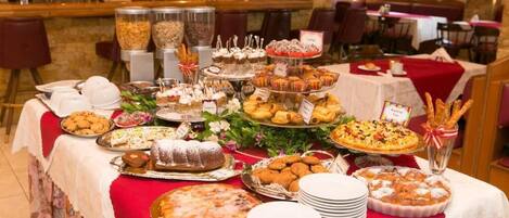 Une table de buffet garnie de divers desserts et pâtisseries, un bar en arrière-plan et une nappe rouge.